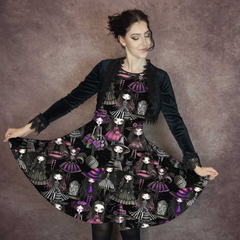 woman wearing a knee length skirt custom printed with spooky dolls in purple and pinks on a brown background. The dress has a gothic vibe