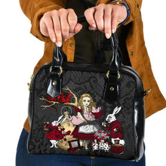 Alice in wonderland black shoulder handbag featuring Alice holding the baby pig watched by the white rabbit and cheshire cat. The bag has a black lace print background and the characters are in red, white and gold. The bag has black handles.