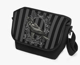 image shows a padded messanger style bag with wide strap. The printed front flap features a gothic grey and black stripe background with a raven motif in black