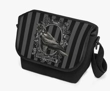 Load image into Gallery viewer, image shows a padded messanger style bag with wide strap.  The printed front flap features a gothic grey and black stripe background with a raven motif  in black 
